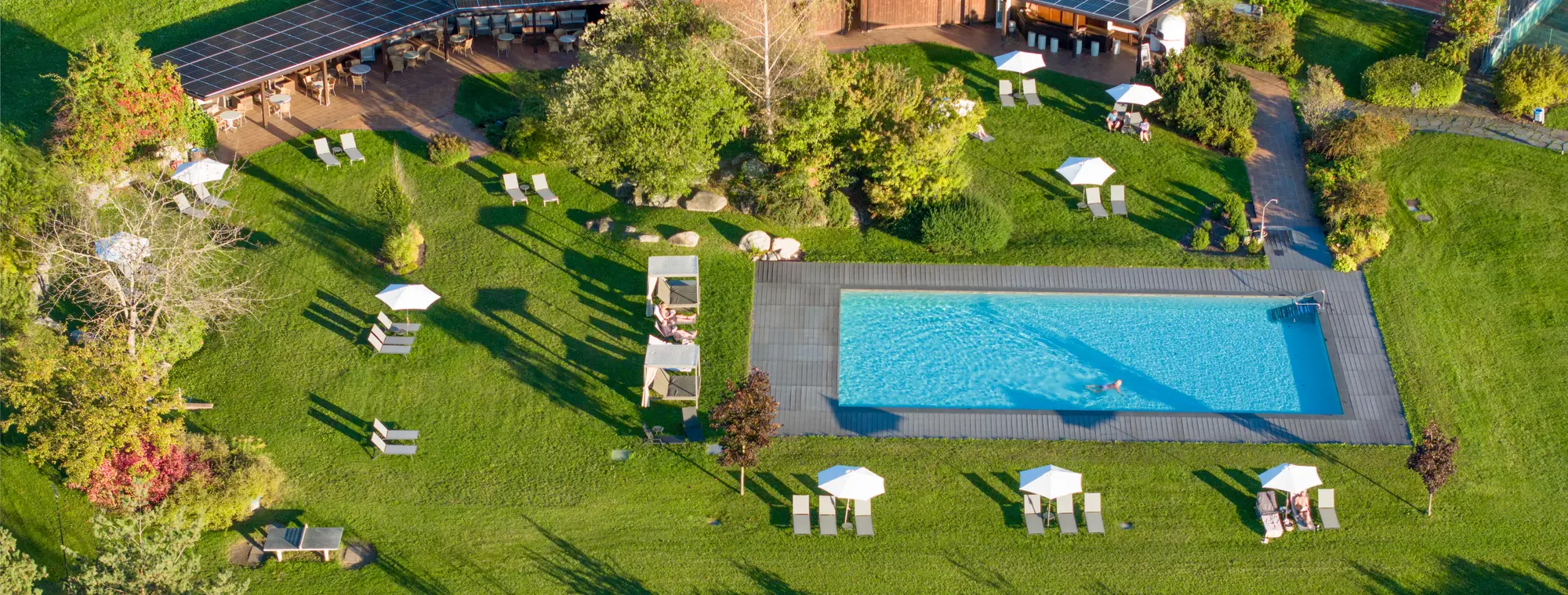 Luftaufnahme Outdoor Pool mit großer Liegefläche und Liegen inkl. Tennisplatz im Hintergrund