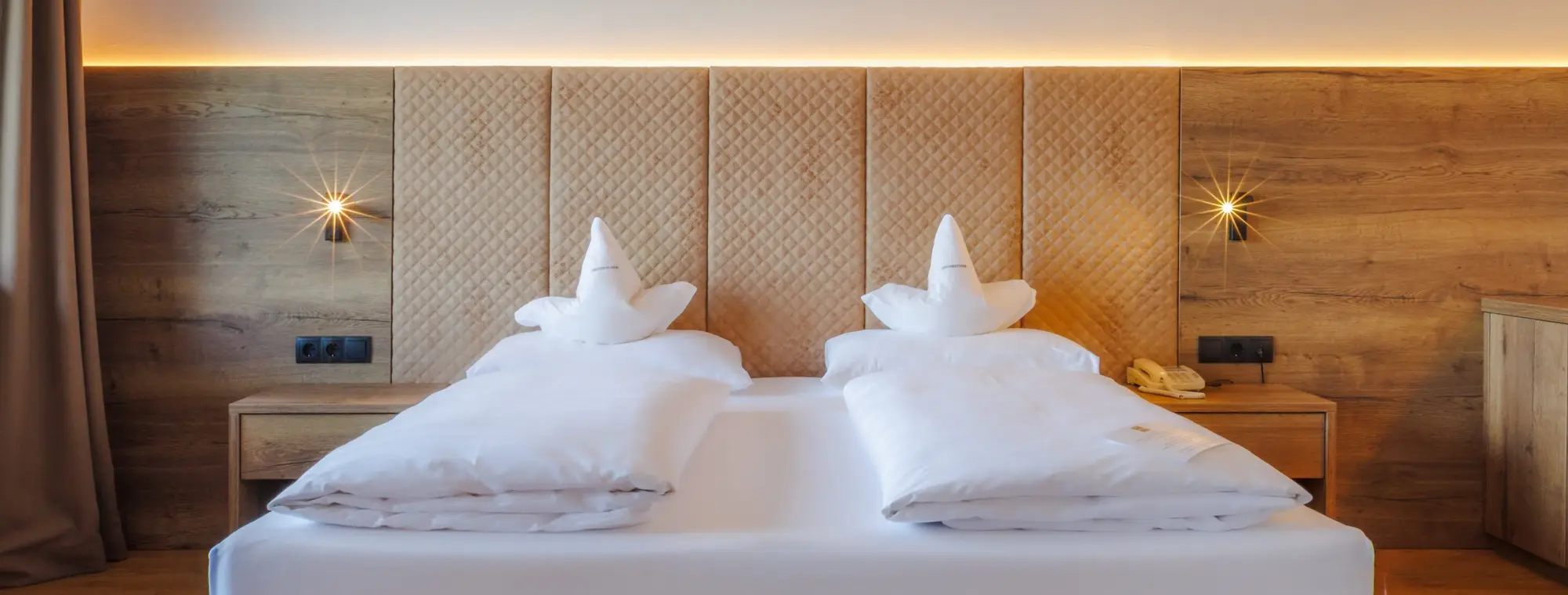 Ein großes Doppelbett mit weißer Bettwäsche und beigen Kopfteil