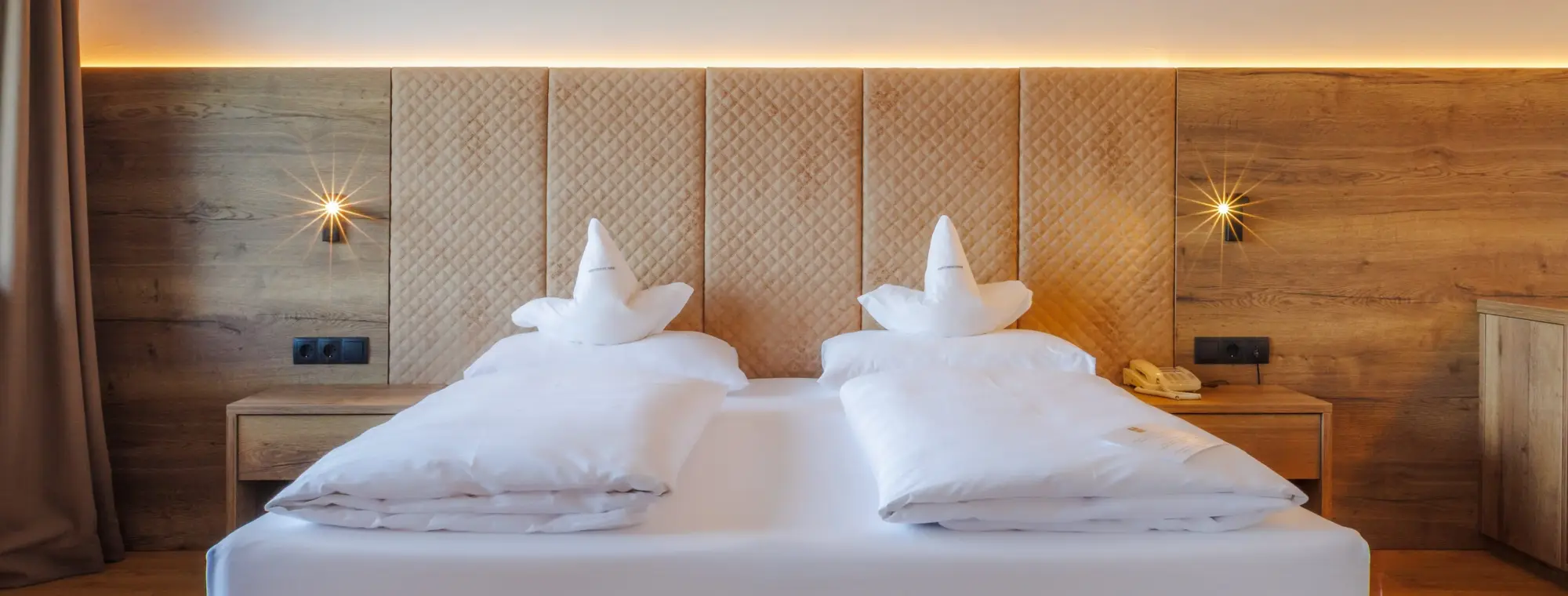 Ein großes Doppelbett mit weißer Bettwäsche und beigen Kopfteil