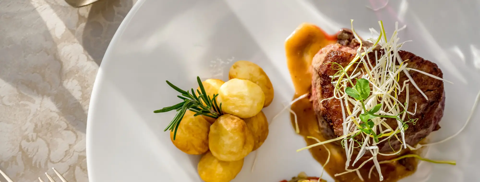 Steak garniert mit Sauce, Gemüsetatar und kleinen Pellkartoffeln. Serviert auf einem großen weißen Teller